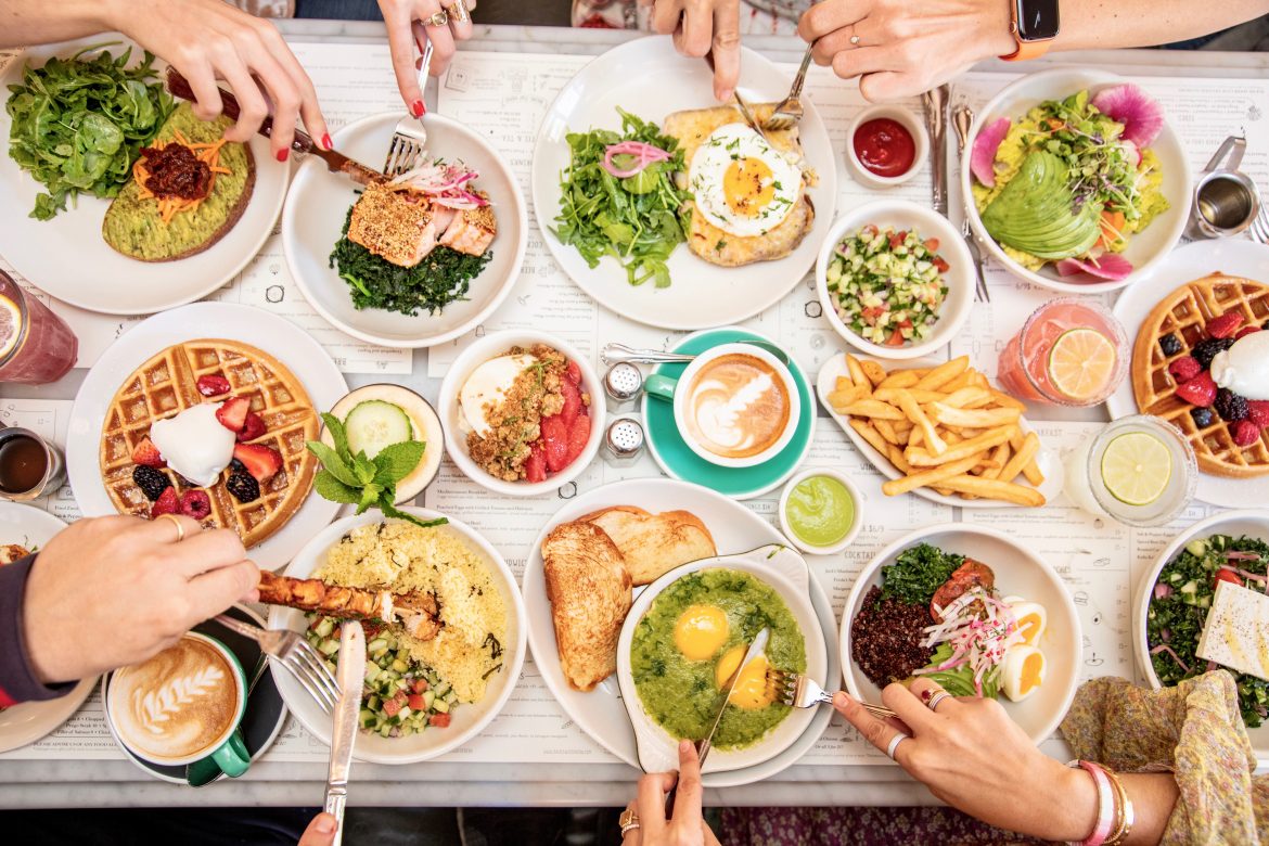 Large table of food and plates with hands grabbing for food