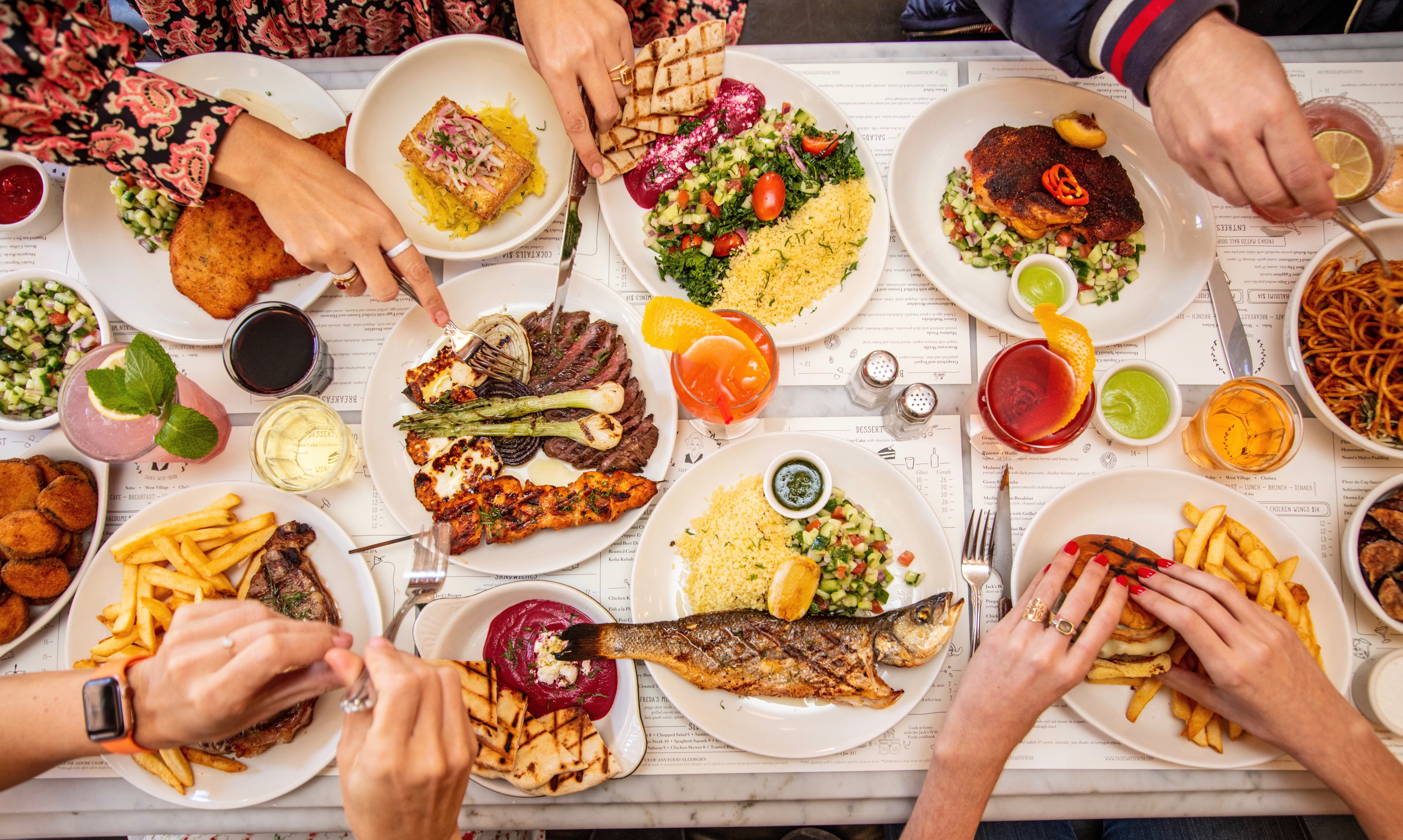 Large table of food and plates with hands grabbing for food